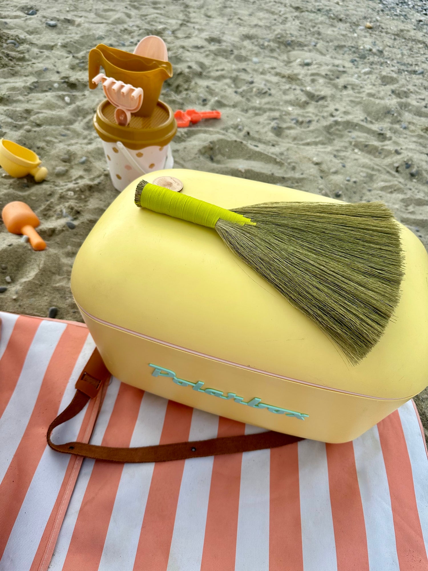 Yellow beach bag with a green anti sand brush on a striped towel at the beach
