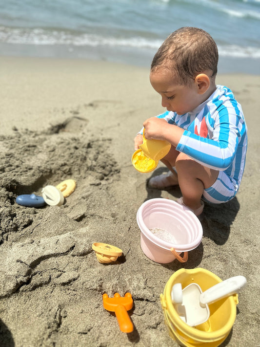 Enfant de 18 mois qui joue dans le sable à la plage avec un seau et une pelle