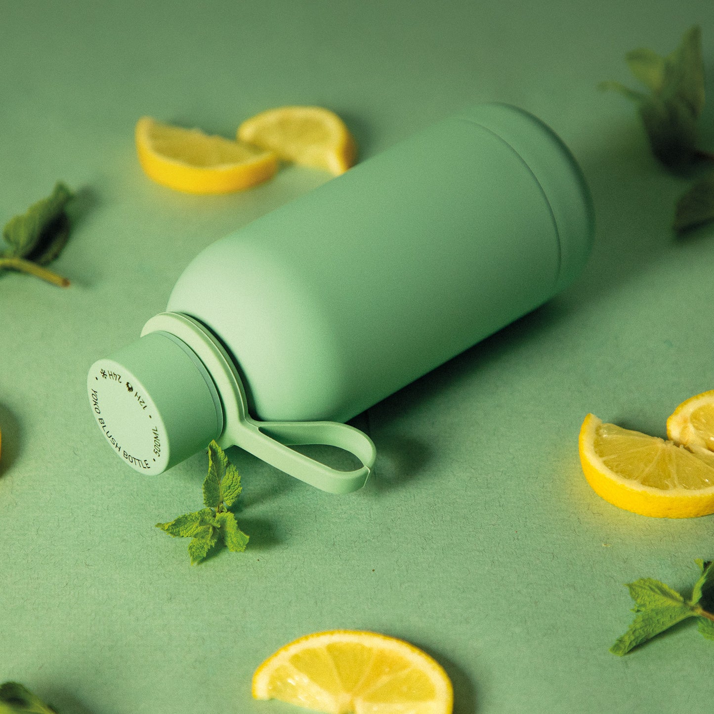 Green insulated water bottle with lemon slices and mint leaves on a green background