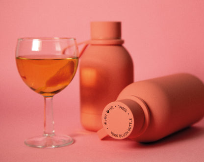 Pink water bottle and glass of pinkish liquid on a pink background